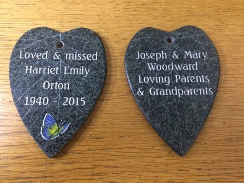 Two heart-shaped stone memorial plaques with engraved inscriptions on a wooden surface.