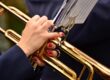 Close-up of hands with red nails playing a golden trumpet, sheet music visible above.