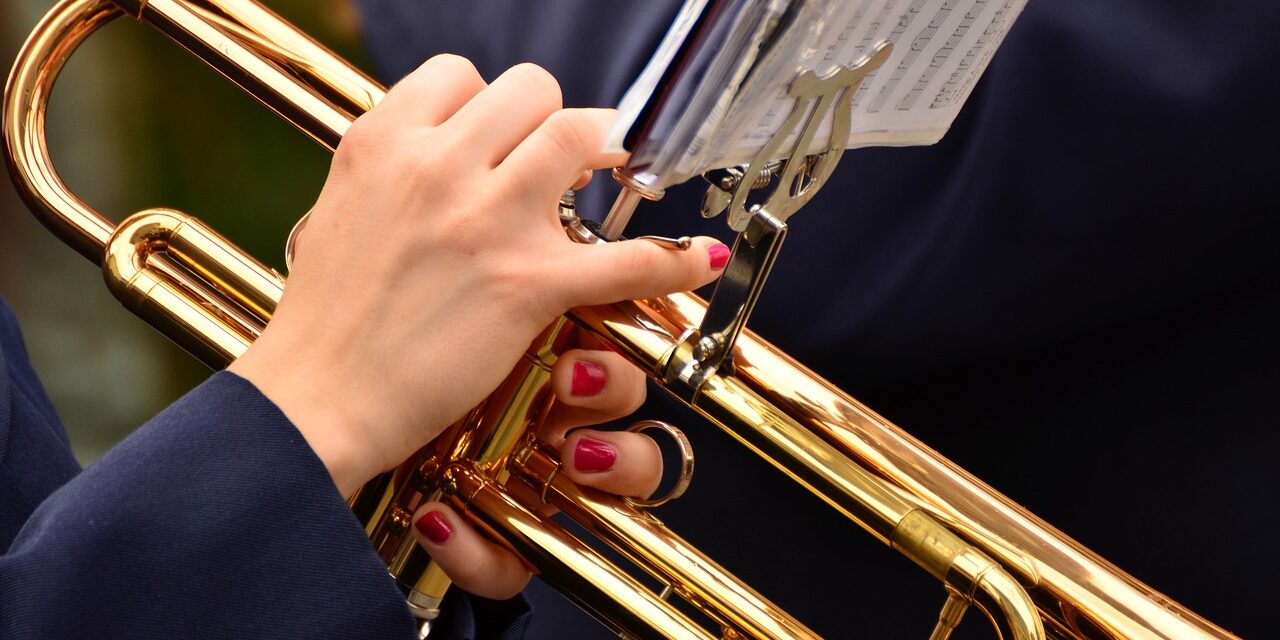 trumpet-3303724_1280 Close-up of hands with red nails playing a golden trumpet, sheet music visible above.
