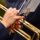 Close-up of hands with red nails playing a golden trumpet, sheet music visible above.