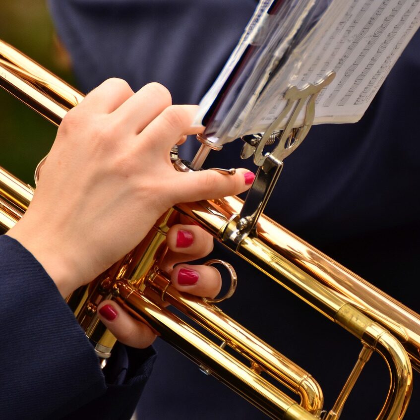 trumpet-3303724_1280 Close-up of hands with red nails playing a golden trumpet, sheet music visible above.