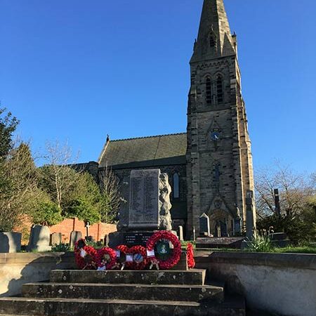West Rainton Church with tall spire behind war memorial decorated with red wreaths on stone steps.